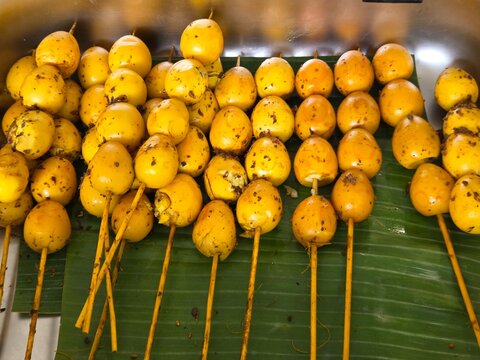 Indonesian traditional skewered quail eggs (Sate Telur Puyuh) seasoned with yellow spices, served on a green banana leaf.