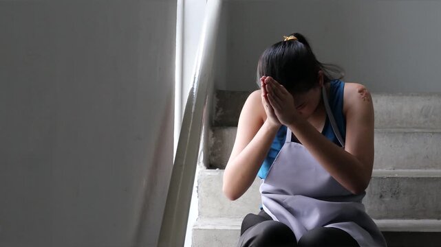Young Adult southeast Asian low-wage worker in prayer on stairwell, Buddhist or Hindu faith in tough times