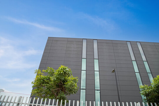 Modern corporate office building facade with dark grey cladding panels and glass windows against blue sky background, low angle view with copy space.