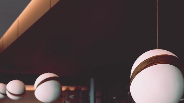 The scene shows multiple round white lamps hanging from the ceiling in a restaurant. The lamps have brown bands around them and cast soft light.