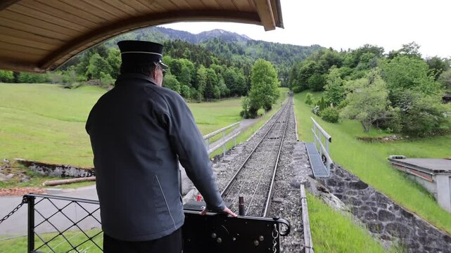 Stans, Nidwalden, Switzerland - 22 August 2026: View of the Stanserhorn-Bahn funicular railway with a conductor operating the train through the green mountain landscape.