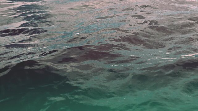Waves flow gently on a beach during the late afternoon. The ocean reflects various colors. Clouds linger in the sky above the water. The scene shows natural movement of the sea.