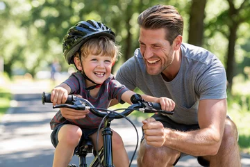 Sunlit park where father and child share joy. Smiling boy grips bike handlebars, helmet secure. Dad crouches close, laughing with proud affection. Green trees frame their playful, carefree moment © lashkhidzetim