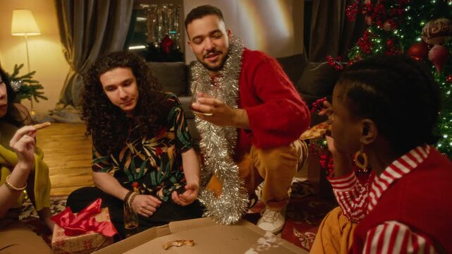 Diverse group of young adults eating pizza, toasting drinks while celebrating Christmas at home. Footage fits holiday party commercials, food delivery ads or festive lifestyle campaigns