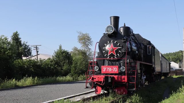 Medvezhyegorsk, Republic of Karelia - 20 August 2026: View of a vintage steam locomotive with a red star on its front parked on the tracks in a rural area.