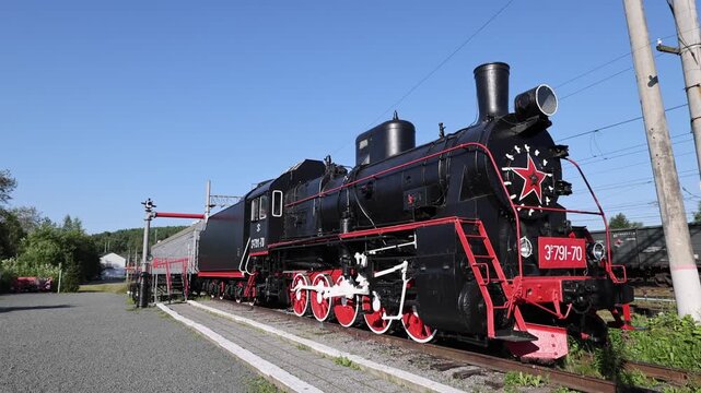 Medvezhyegorsk, Republic of Karelia, Russia - 20 August 2026: View of a black steam locomotive with red wheels and a red star on the front parked on railway tracks.