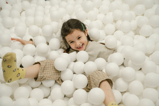 Young girl laughs joyfully while playing in a ball pit filled with soft white balls
