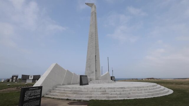 Wakkanai, Hokkaido, Japan - 19 August 2026: View of the Tower of Prayer monument at Cape Soya, featuring a tall white stone spire on a circular base in a grassy coastal field.