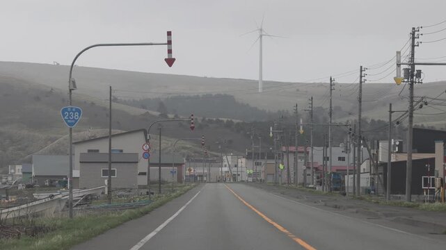 Wakkanai, Hokkaido, Japan - 19 August 2026: View of a quiet road in Wakkanai with a wind turbine on the distant hill under an overcast sky.