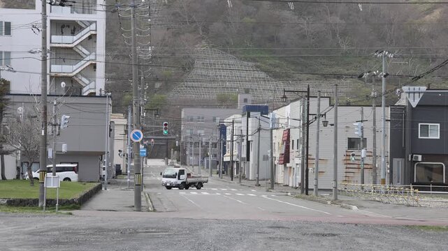 Wakkanai, Japan - 19 August 2026: View of a quiet street with buildings, utility poles, and a small van driving along the road in Hokkaido.