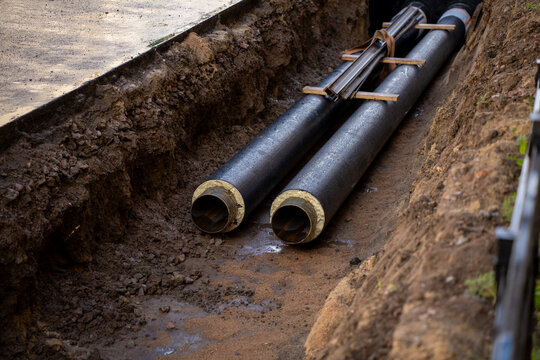 Two pre insulated industrial utility pipes laid inside an open ground trench during urban pipeline replacement and heating system infrastructure construction.