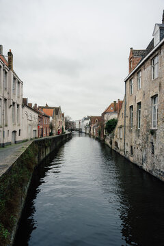 Bruges, Flanders, Belgium - 03 February 2024: View of the historic canal in Bruges lined with traditional brick buildings under a cloudy sky.