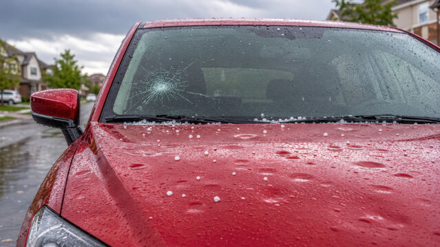 Hail damaged windshield on a parked red car after violent weather, vehicle repair costs, comprehensive auto insurance coverage