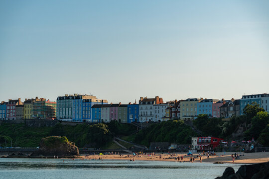 Tenby, Wales, United Kingdom - 01 August 2024: View of colorful historic buildings on the cliffside above the sandy beach and harbour, with people enjoying the sunny summer day.
