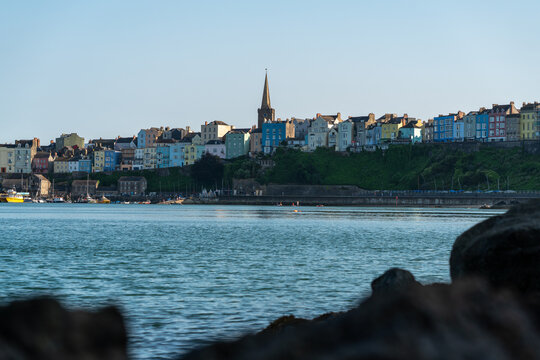 Tenby, United Kingdom - 01 August 2024: View of the colorful historic houses and church spire overlooking the harbor in Tenby, Wales, United Kingdom.