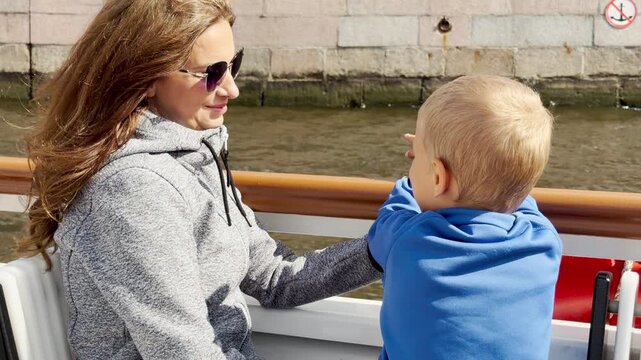 A loving mother and curious boy enjoy a boat ride along a stone canal wall in Saint Petersburg. This joyful family moment brings warm feelings of peace.