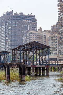 An old pier on the bank of the Nile, with high-rise apartment buildings of Cairo beyond, the rooftop adorned with hundreds of satellite dishes. Cairo is the capital and largest city in Egypt.