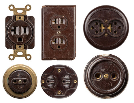 A collection set of various vintage bakelite and brass electrical power sockets and outlets featuring circular, duplex, and surface-mounted designs with a weathered patina, isolated