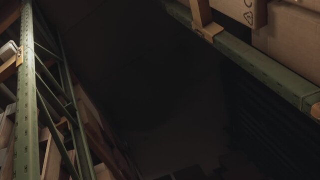 Shelves are filled with boxes in a storage area of a warehouse. Light comes from above. The space is organized but narrow, showing only a portion of the area.