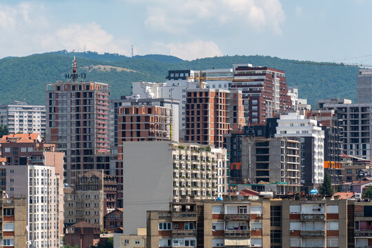 Pristina, Kosovo - 19 June 2025: View of the modern urban skyline with various high-rise apartment buildings and construction sites set against green hills.
