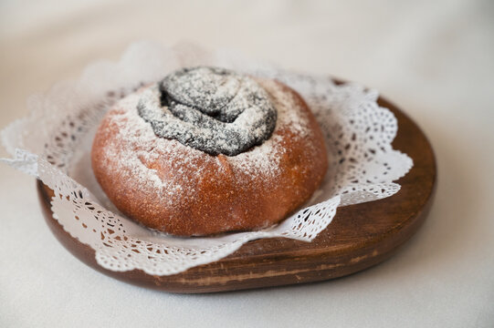 Fresh baked poppy seed bun dusted with powdered sugar, served on wooden plate with lace napkin in cozy minimalist setting.