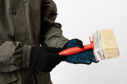 Close-up of a worker wearing gloves and holding a wide paint brush, illustrating home renovation, decorating and construction work.