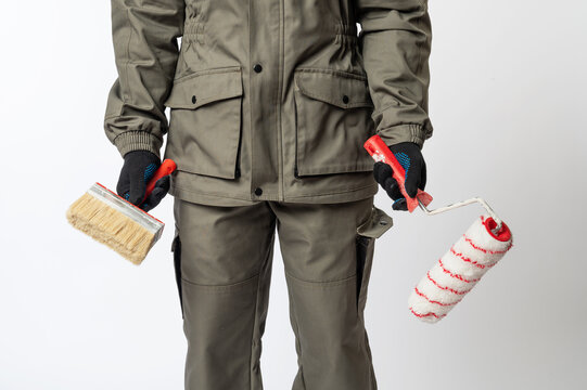 Construction worker in protective clothing holding paint brush and roller, ready for home renovation, decorating or professional painting work.