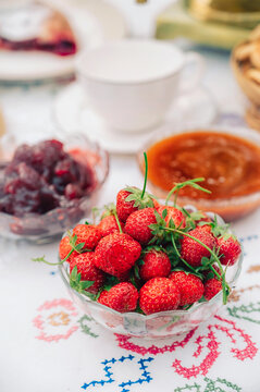 Homemade cherry pie slice with powdered sugar served with fresh strawberries, fruit preserves and tea on a cozy table setting.