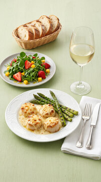 Gratin&eacute;ed scallops in cheese sauce with grilled asparagus, arugula salad, strawberries, and mango; served with a bread basket and a glass of white wine