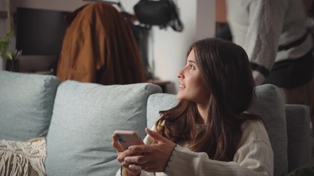 Young Latino couple looking at a smartphone together on their sofa, representing connection, shared technology, relationships, and modern home lifestyle.
