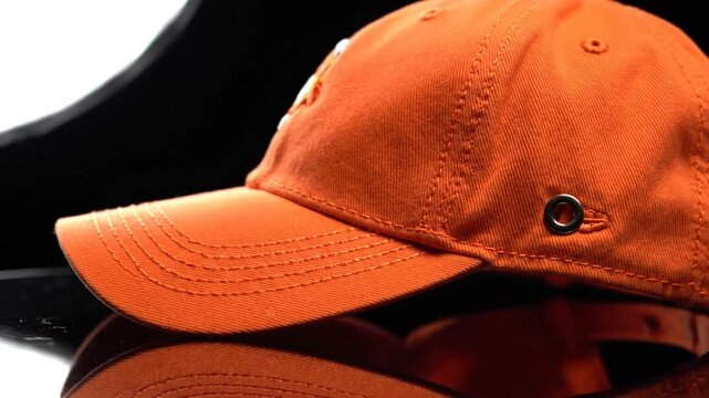Orange baseball cap with reflection on dark background