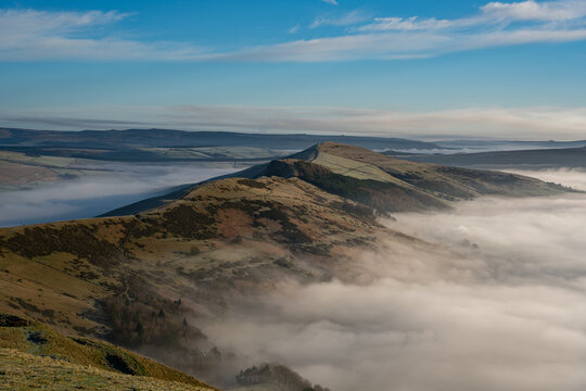 View of Mam Tor rising above a sea of morning mist covering the rolling hills of the Peak District in Hope Valley, England, United Kingdom.