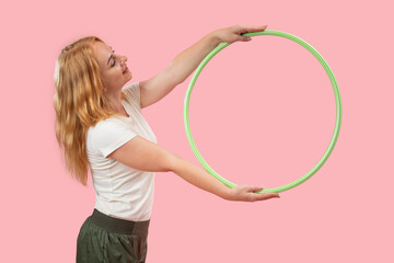 Blonde woman smiling, holding a green hula hoop on a pink background, representing concepts of sport, healthy lifestyle, physical activity, wellbeing, and women's health through play and exercise © somemeans