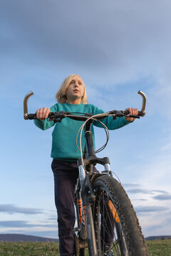 Young boy riding a mountain bike outdoors, looking thoughtfully towards the horizon, symbolizing exploration, freedom, and an active childhood under a clear sky