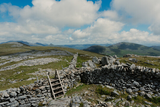 View of the rugged Nantlle Ridge landscape featuring a traditional dry stone wall with a wooden stile, set against rolling hills in Nantlle, Wales, United Kingdom.