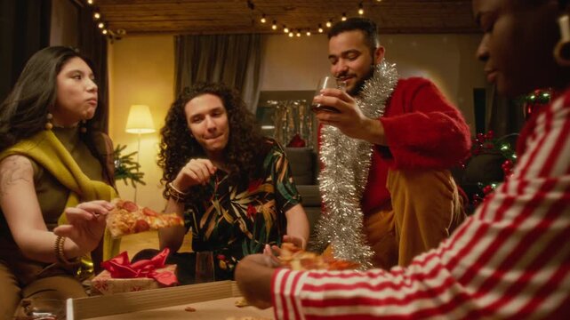 Diverse multiethnic young friends celebrating Christmas, eating pizza, and toasting with drinks at home. Clip suited for food delivery marketing and holiday promotions