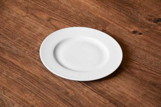 Ceramic white flat plate for food on wooden table top view