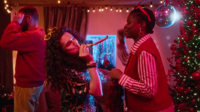 Caucasian young man blowing party blower while dancing with African American woman at holiday party. Clip suitable for festive marketing campaigns and seasonal advertising projects