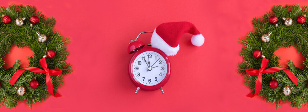 Alarm clock with Santa hat and Christmas wreath on a red background. Top view. Copy space.