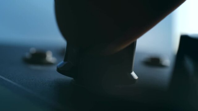 Close up shot of a hand adjusting a black control knob on a professional audio device, regulating volume or frequency settings on a mixing console or amplifier for sound mixing and recording