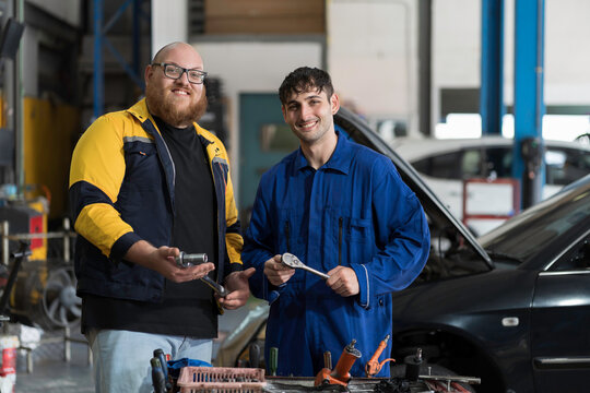 Two male mechanic working, inspects and repairs car engine and components with hood open inside services garage. Car repair services concept, Auto garage
