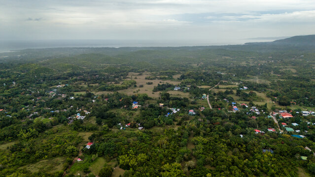 Aerial view of the lush landscape of Siquijor, featuring scattered houses, dense vegetation, rolling hills, and a distant coastline in Siquijor, Central Visayas, Philippines.