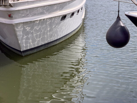 Black Rubber Boat Fender Hanging Beside Moored White Yacht Hull at Marina Dock