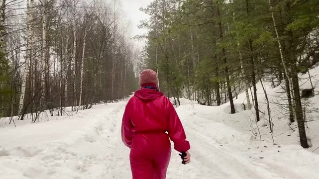 Young woman in red jacket walking along snowy path in dense forest.