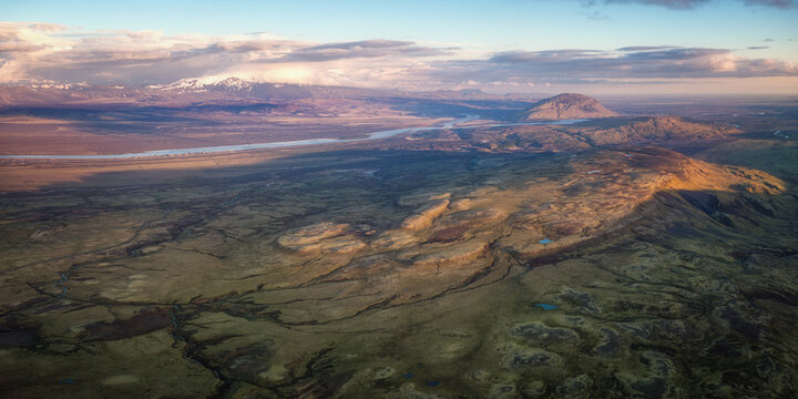Aerial view of the rugged volcanic landscape near Haifoss with mossy hills, winding rivers, and snow-capped mountains under golden hour light in Skeida- og Gnupverjah, Iceland.