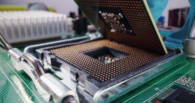 Tracking macro shot of gloved hand inserting cpu processor into motherboard socket on electronics workstation.