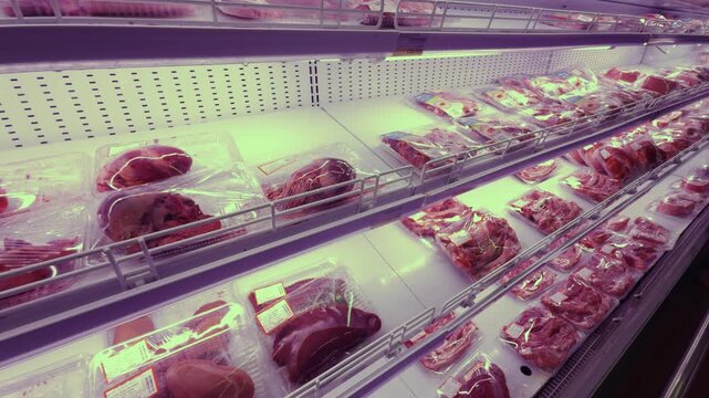 Various raw fresh meat cuts, including beef and pork, displaying in transparent plastic packaging on a refrigerated shelf inside a supermarket, representing food retail and consumer shopping