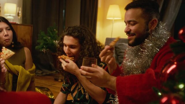 Multiethnic young friends eating pizza and drinking during Christmas party at home. Clip suitable for festive holiday advertising, fast food delivery promotions and lifestyle campaigns