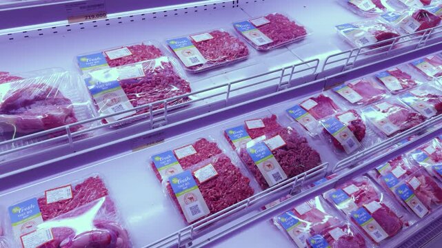 Supermarket refrigerated display case presenting an abundant selection of fresh raw red meat, including ground beef and other protein cuts, neatly organized in plastic packaging