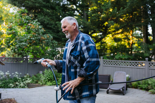 Smiling senior man watering backyard garden with hose